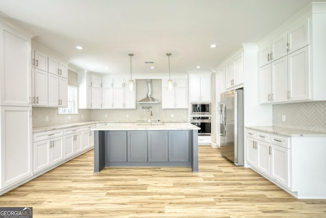 kitchen with wall chimney exhaust hood, appliances with stainless steel finishes, hanging light fixtures, light stone countertops, and white cabinetry