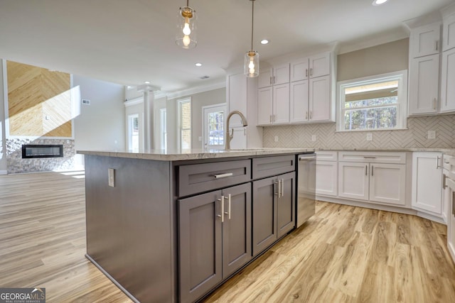 kitchen featuring a center island with sink, white cabinets, open floor plan, hanging light fixtures, and stainless steel dishwasher