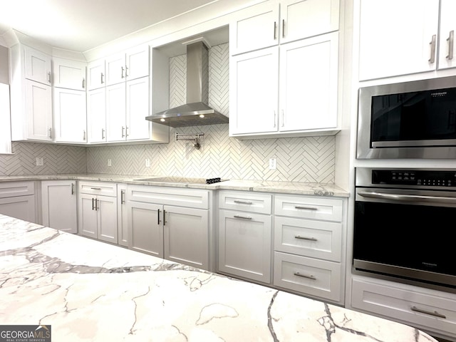 kitchen with black electric cooktop, oven, white cabinets, built in microwave, and wall chimney exhaust hood