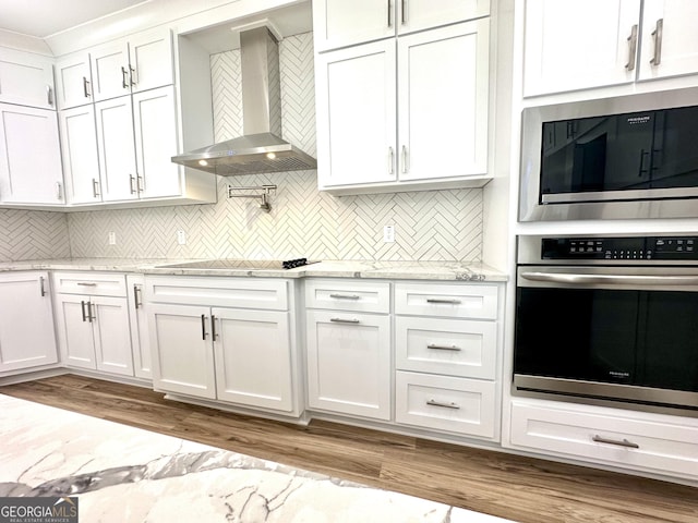 kitchen with built in microwave, white cabinets, stainless steel oven, and wall chimney exhaust hood