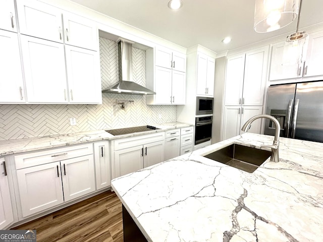 kitchen featuring white cabinets, wall chimney exhaust hood, decorative light fixtures, stainless steel appliances, and a sink