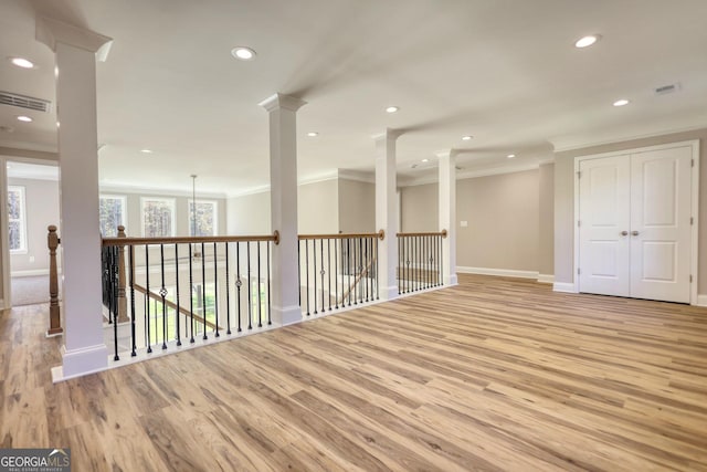 spare room with light wood-type flooring, decorative columns, and crown molding