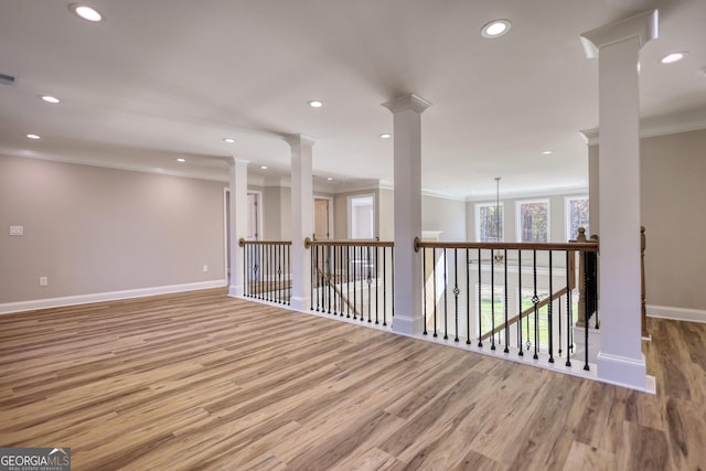 spare room with crown molding, light wood finished floors, and ornate columns