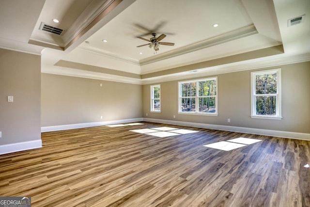 unfurnished room with wood finished floors, a raised ceiling, visible vents, and crown molding