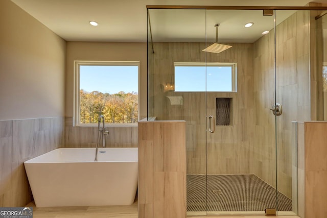 bathroom featuring a stall shower, a wainscoted wall, a freestanding tub, tile walls, and recessed lighting