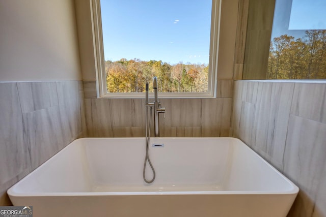 full bath featuring a freestanding bath, a sink, and tile walls