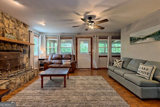 living room with a stone fireplace, ceiling fan, plenty of natural light, and dark hardwood / wood-style floors