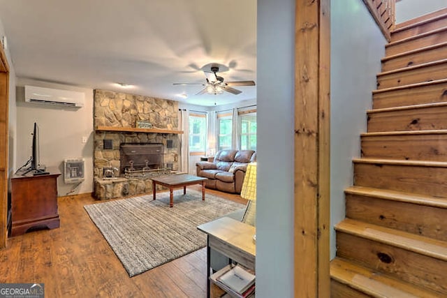 living room with a wood stove, ceiling fan, an AC wall unit, heating unit, and hardwood / wood-style floors