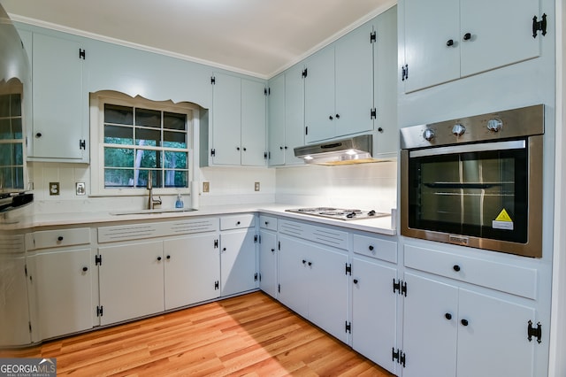 kitchen featuring stainless steel oven, white gas stovetop, backsplash, sink, and light wood-type flooring