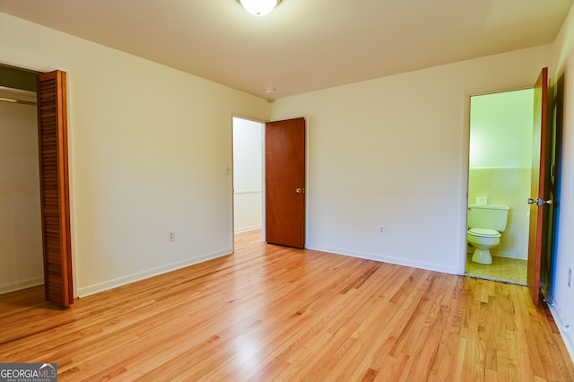 unfurnished bedroom with connected bathroom, a closet, light hardwood / wood-style floors, and tile walls