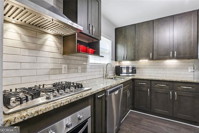 kitchen with stainless steel appliances, a sink, wall chimney range hood, and light stone counters