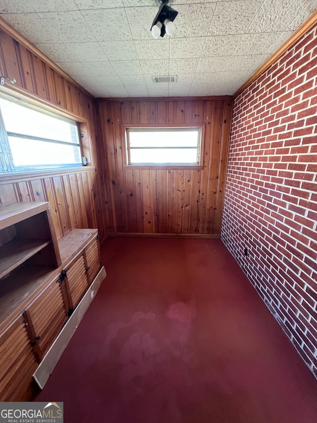 interior space with a paneled ceiling, dark carpet, wooden walls, and brick wall