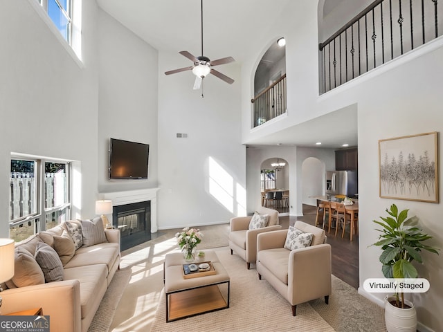 living room featuring ceiling fan, a towering ceiling, and light hardwood / wood-style flooring