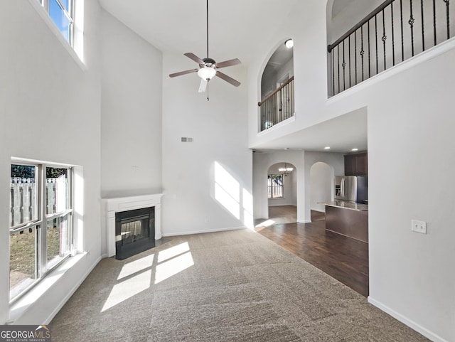 unfurnished living room featuring a high ceiling, dark hardwood / wood-style floors, plenty of natural light, and ceiling fan