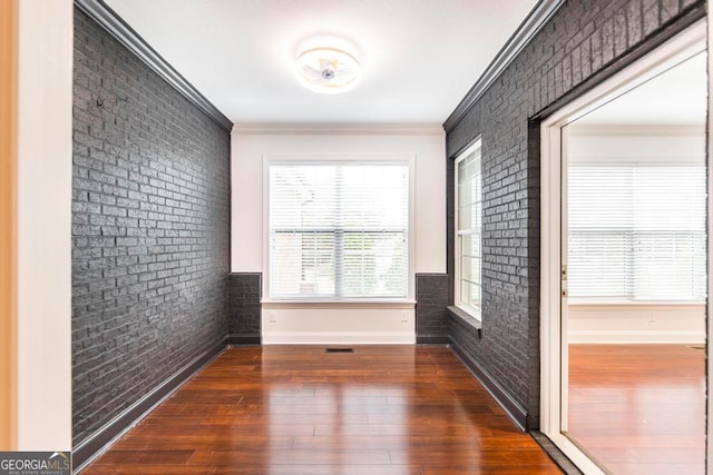 empty room with ornamental molding, dark wood-type flooring, and brick wall