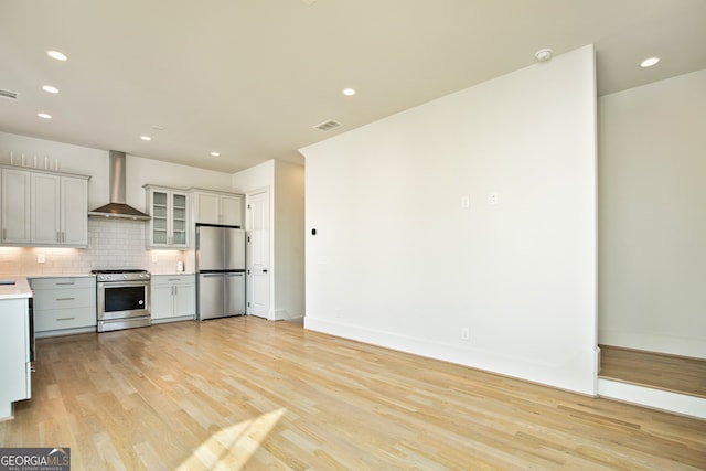 kitchen with backsplash, wall chimney exhaust hood, light hardwood / wood-style floors, stainless steel appliances, and gray cabinets