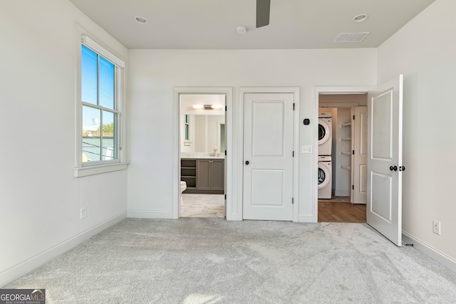 unfurnished bedroom with light colored carpet, stacked washer / dryer, and ensuite bathroom