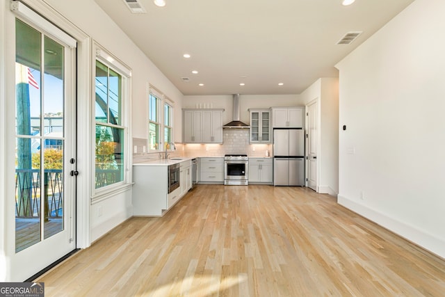 kitchen with sink, stainless steel appliances, wall chimney range hood, backsplash, and light hardwood / wood-style floors