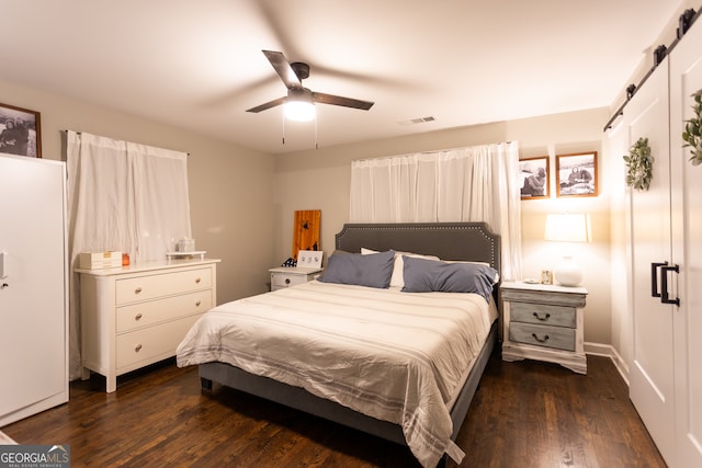 bedroom with a barn door, ceiling fan, and dark hardwood / wood-style flooring