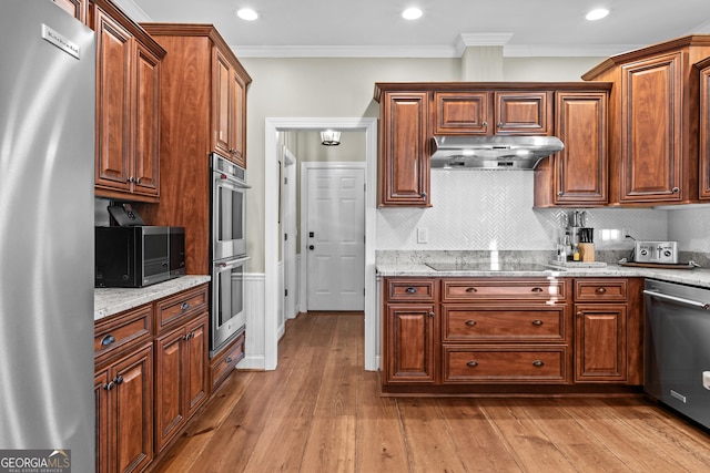 kitchen with appliances with stainless steel finishes, decorative backsplash, light hardwood / wood-style floors, light stone counters, and crown molding