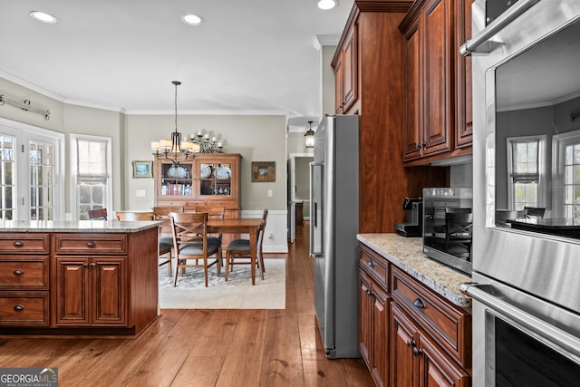 kitchen with hanging light fixtures, ornamental molding, stainless steel fridge, a notable chandelier, and light stone countertops