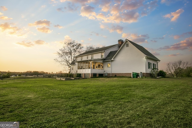 back house at dusk featuring a yard and a sunroom