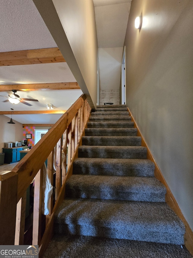 staircase with ceiling fan and beamed ceiling