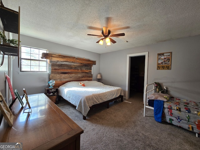 bedroom with ceiling fan, dark carpet, a walk in closet, and a textured ceiling