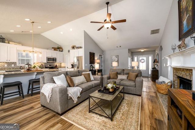 living room featuring a fireplace, high vaulted ceiling, ceiling fan, and light wood-type flooring