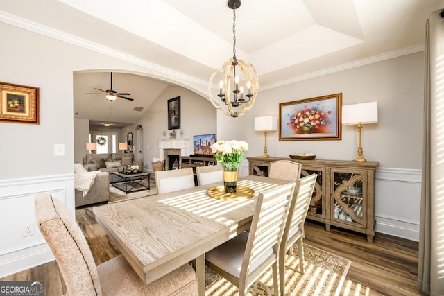 dining room with hardwood / wood-style flooring, ceiling fan with notable chandelier, a raised ceiling, and crown molding