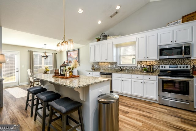 kitchen with a center island, appliances with stainless steel finishes, hanging light fixtures, white cabinets, and vaulted ceiling