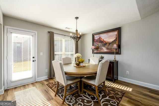 dining space with wood-type flooring, a wealth of natural light, and an inviting chandelier