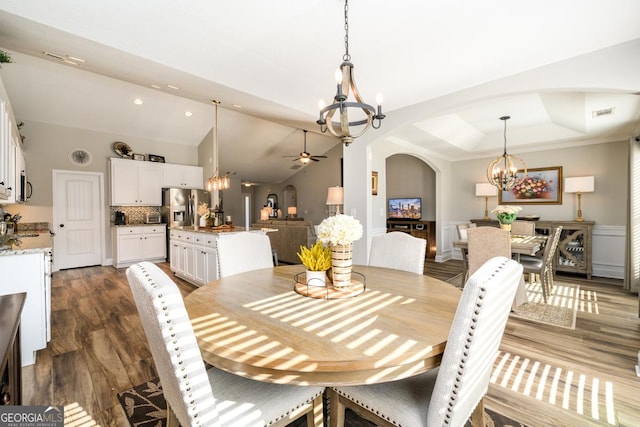 dining space featuring a raised ceiling, ornamental molding, ceiling fan with notable chandelier, dark hardwood / wood-style floors, and lofted ceiling