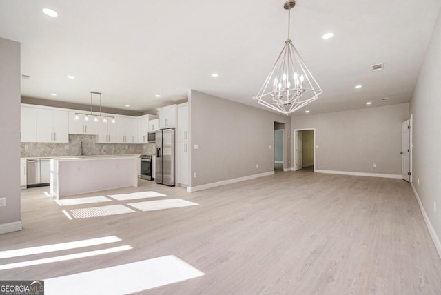 unfurnished living room featuring an inviting chandelier and light hardwood / wood-style flooring