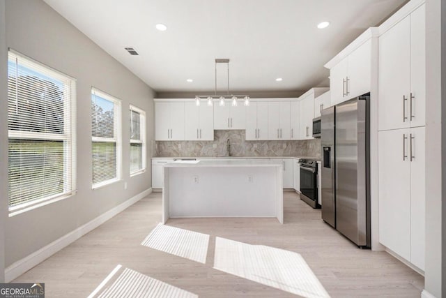 kitchen with pendant lighting, a kitchen island, white cabinets, and appliances with stainless steel finishes