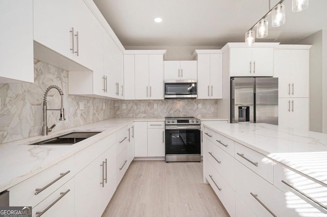 kitchen featuring sink, appliances with stainless steel finishes, pendant lighting, white cabinets, and light wood-type flooring