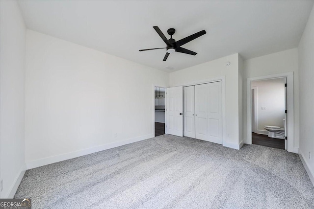 unfurnished bedroom featuring ceiling fan, dark carpet, ensuite bathroom, and a closet