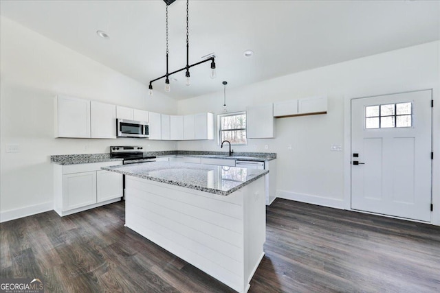 kitchen featuring appliances with stainless steel finishes, light stone counters, pendant lighting, a center island, and white cabinetry