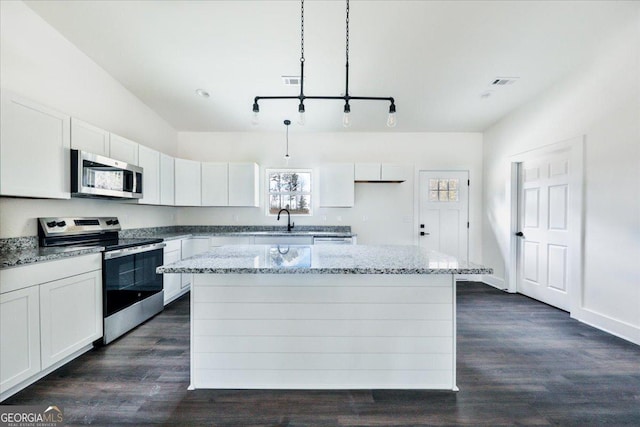 kitchen featuring a center island, light stone countertops, decorative light fixtures, white cabinetry, and stainless steel appliances