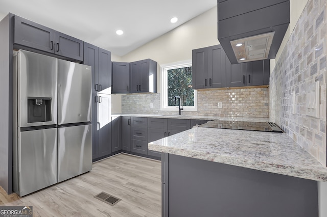 kitchen featuring sink, light stone counters, stainless steel refrigerator with ice dispenser, decorative backsplash, and light wood-type flooring