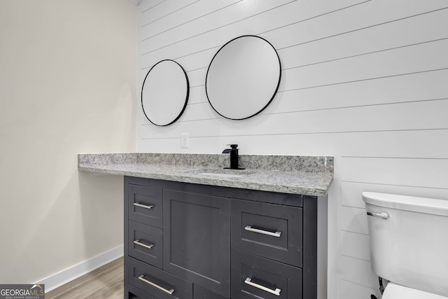 bathroom featuring hardwood / wood-style floors, vanity, toilet, and wood walls