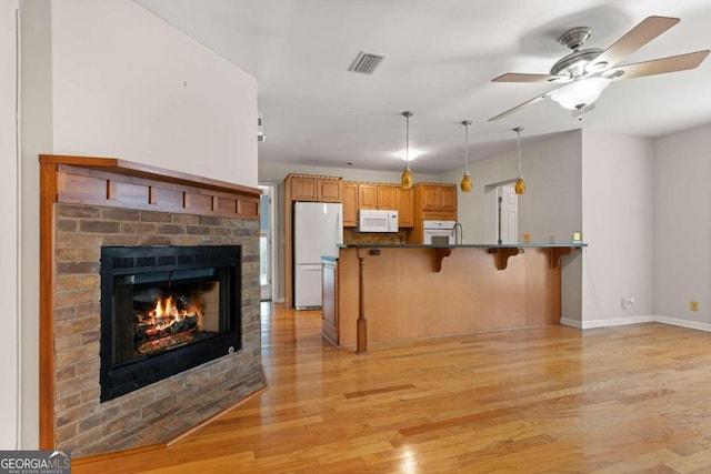 kitchen with kitchen peninsula, a kitchen breakfast bar, white appliances, light hardwood / wood-style flooring, and a fireplace