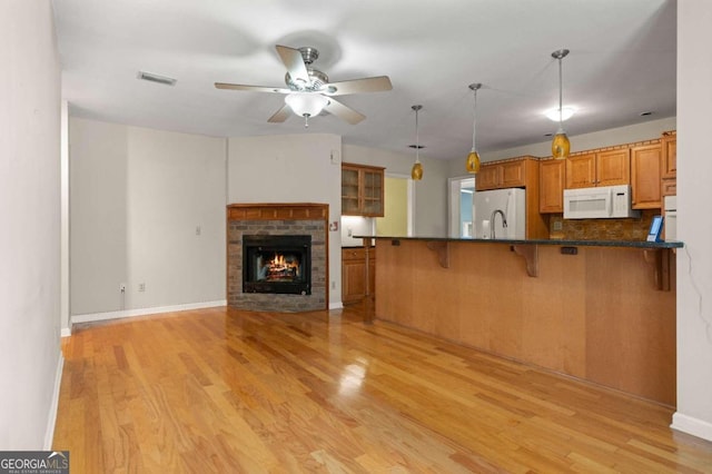 kitchen with white appliances, decorative light fixtures, a fireplace, light hardwood / wood-style floors, and a breakfast bar area