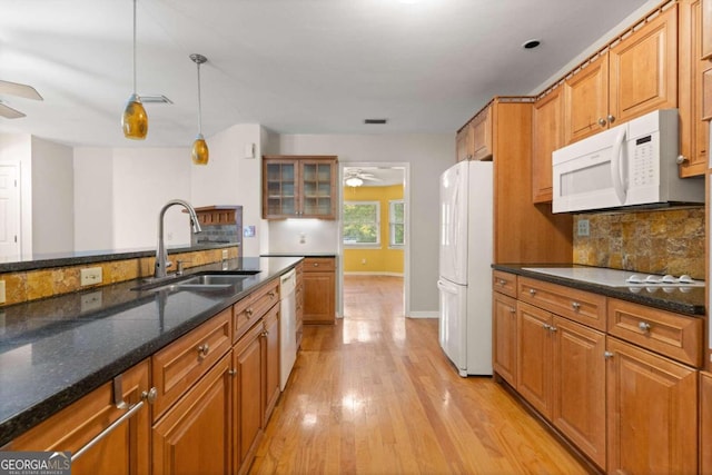 kitchen featuring sink, hanging light fixtures, dark stone counters, light hardwood / wood-style floors, and white appliances