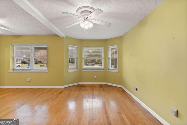 spare room with ceiling fan, beamed ceiling, a textured ceiling, and light wood-type flooring