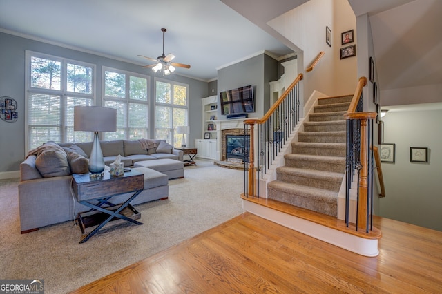 living room with hardwood / wood-style floors, a stone fireplace, ceiling fan, and crown molding