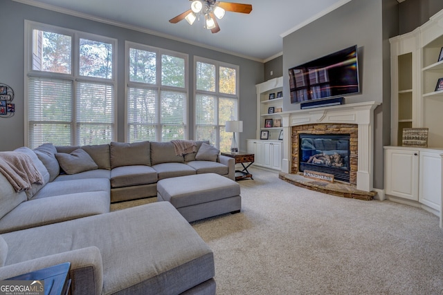 carpeted living room with crown molding, ceiling fan, a healthy amount of sunlight, and a stone fireplace