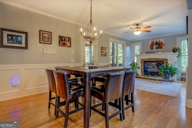 dining area featuring light hardwood / wood-style floors, a stone fireplace, ornamental molding, and a wealth of natural light