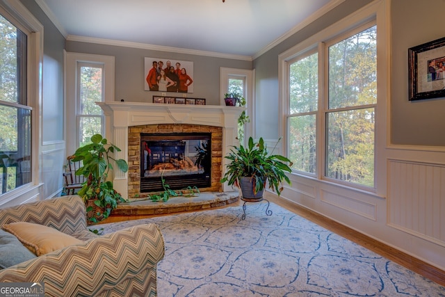 sitting room featuring a stone fireplace, ornamental molding, a healthy amount of sunlight, and hardwood / wood-style flooring