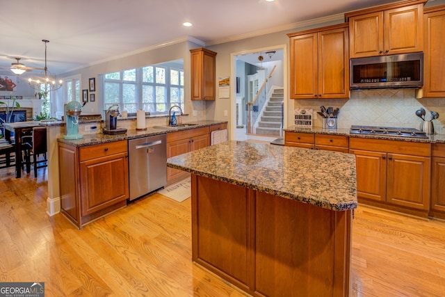 kitchen with appliances with stainless steel finishes, light wood-type flooring, sink, a center island, and hanging light fixtures